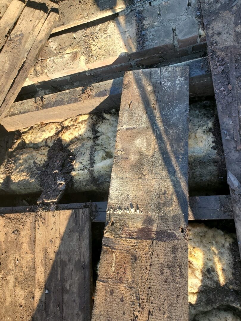 Old pipes beneath wooden floorboards showing wear and rust.