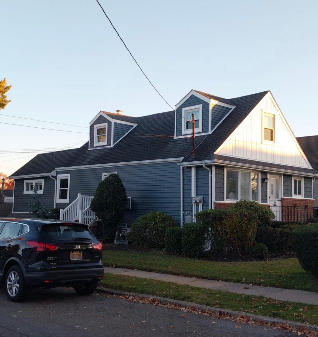 A blue house with dormer windows and a black car parked outside.
