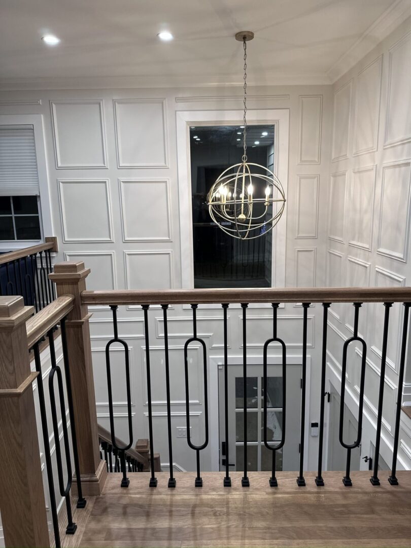 Elegant staircase with modern chandelier and white paneled walls.