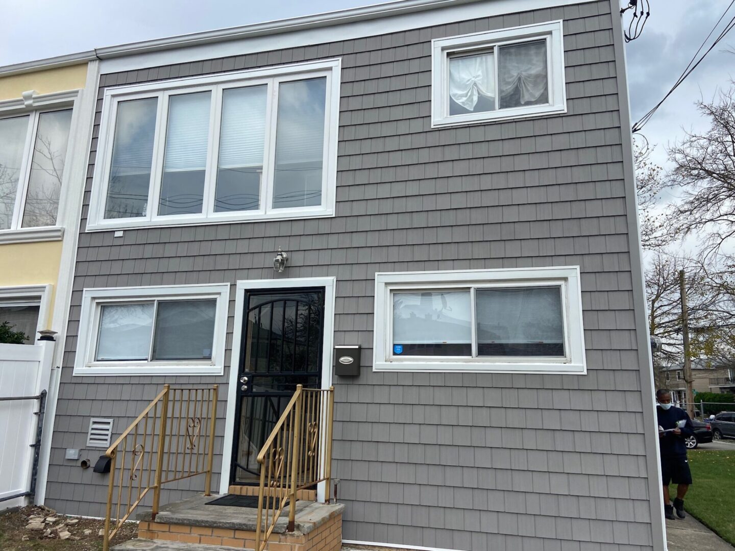 Gray two-story house with barred windows and a front door with a metal security gate.