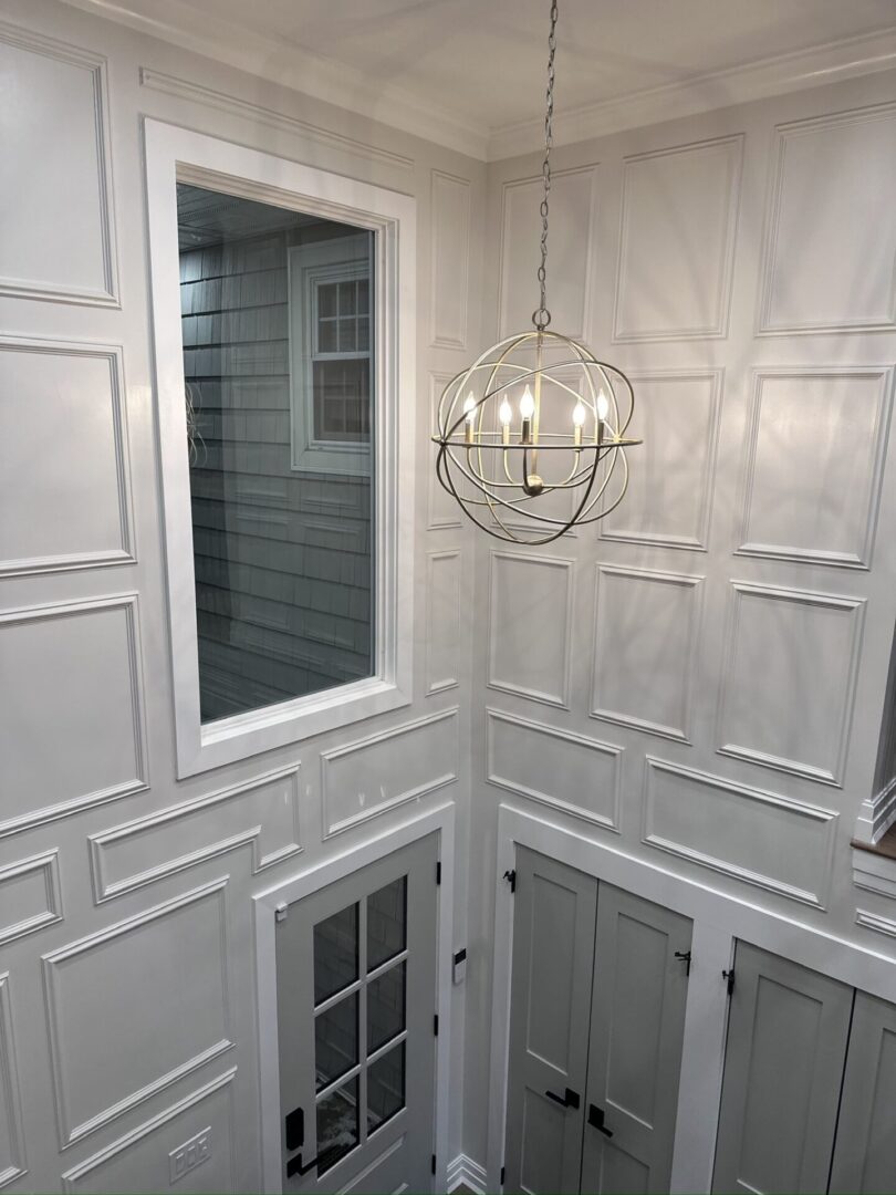 Elegant white paneled walls and a modern chandelier in a stairwell.
