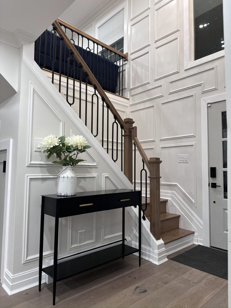 Elegant staircase with wooden railing and black console table with white flowers.
