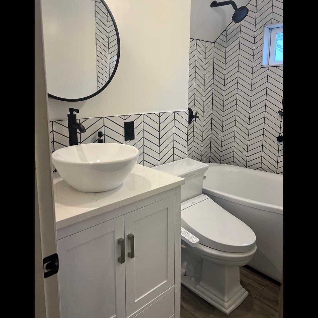 Modern bathroom with white vanity, round mirror, and patterned tile shower.