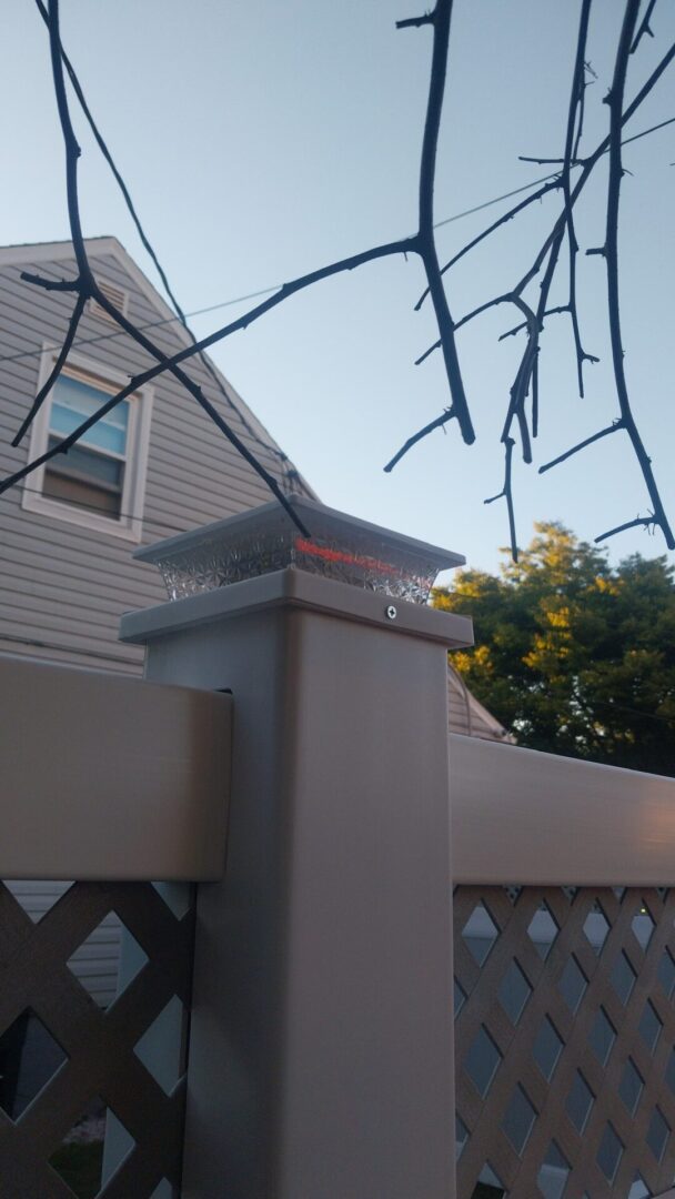 View of a house roof and fence post with a bare tree branch in foreground.