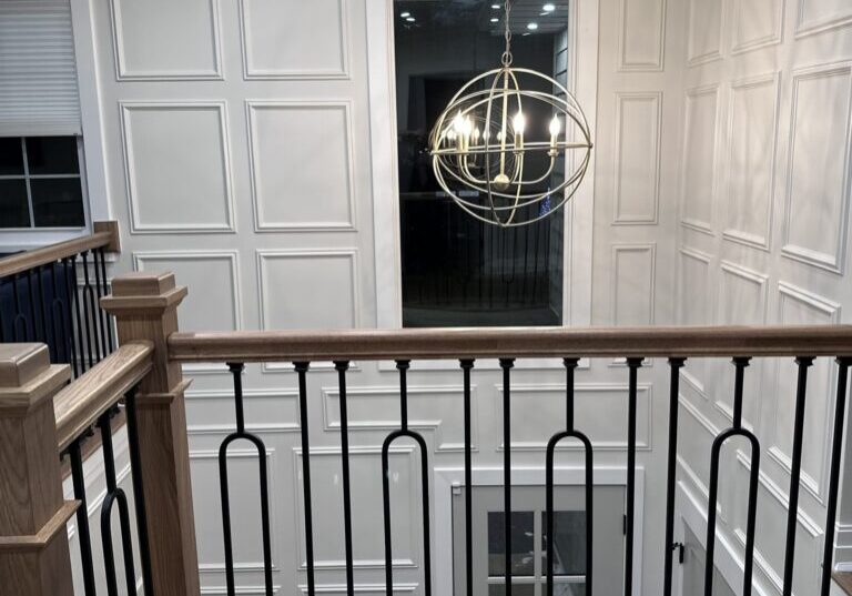Elegant white paneled walls with a modern spherical chandelier above a staircase.